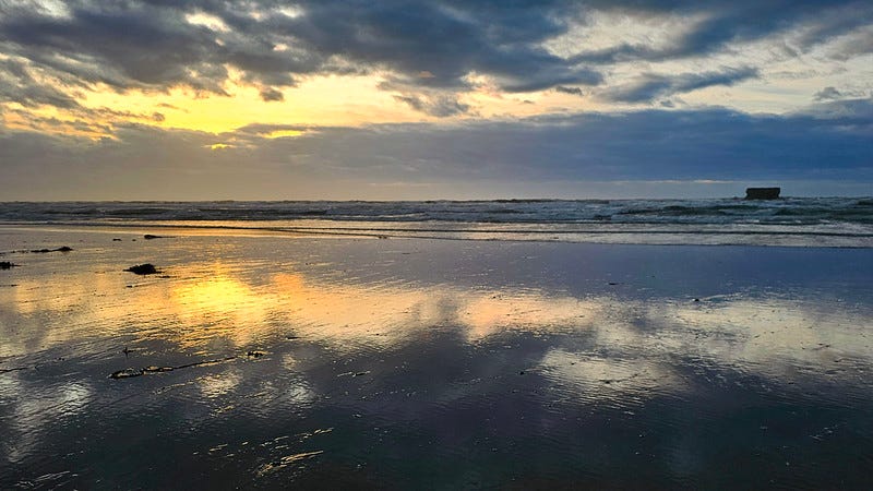 Scène de plage avec le ciel reflété dans le sable mouillé.