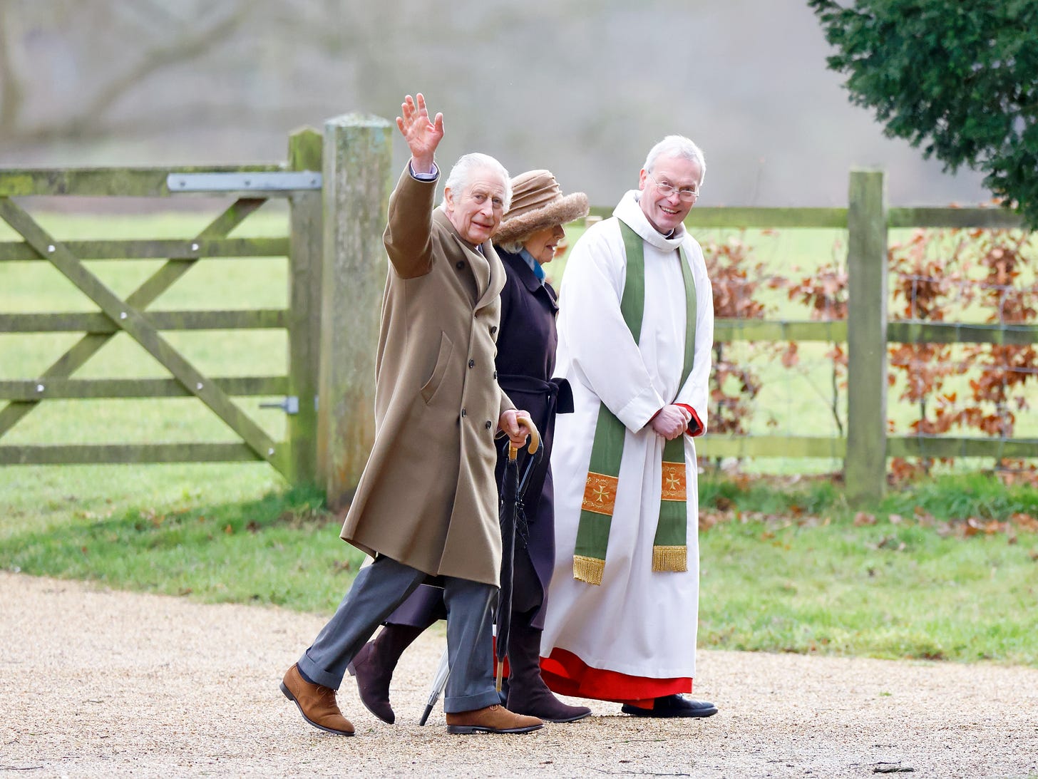 King Charles waving with Camilla and a vicar outside