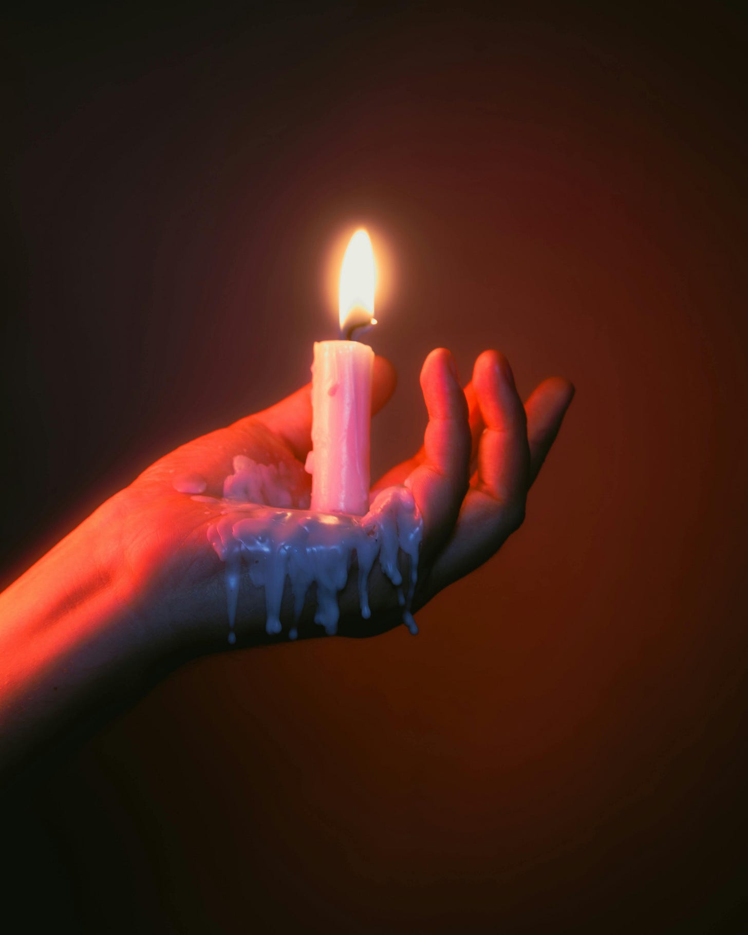 A hand holding a candle whose wax is melting in a red glowing room