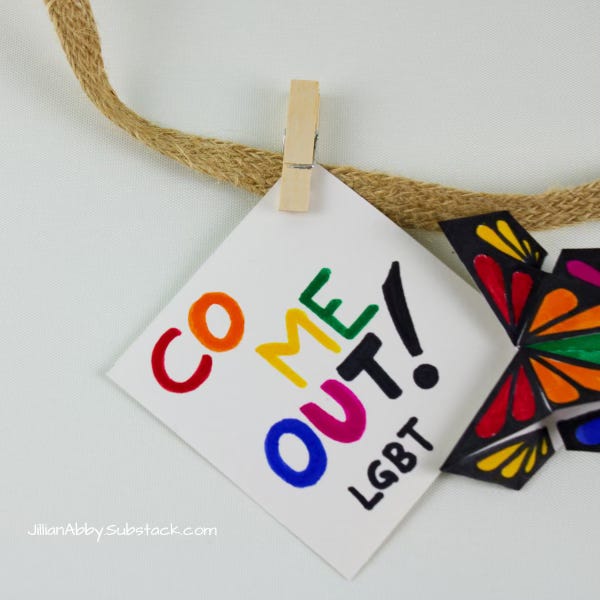 brown woven clothes lines with a wooden clothespin holding a small sign that says "Come Out LGBT" along with a paper multicolored butterfly.