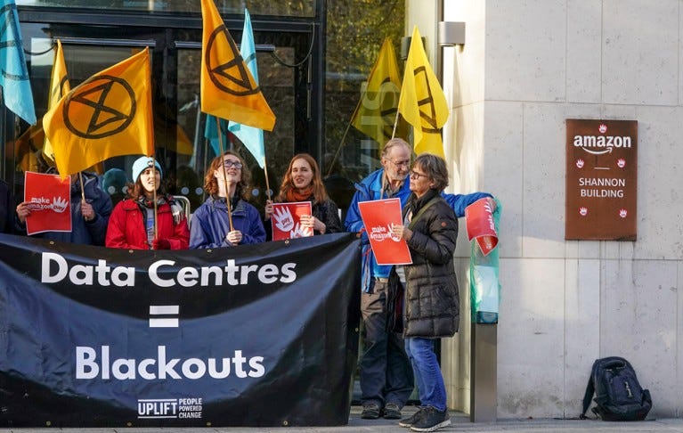 Protesters outside Amazon headquarters holding extinction rebellion flags and a banner reading "Data Centres = Blackouts"