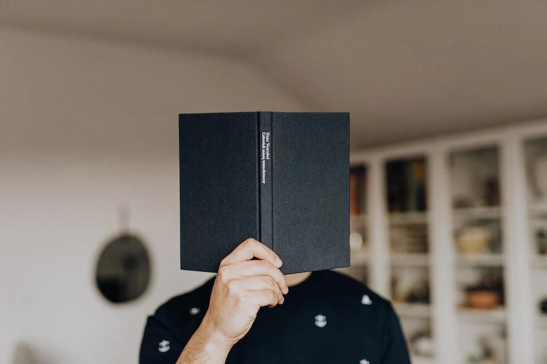 Pexels photo of man behind a book by Karolina Grabowska.