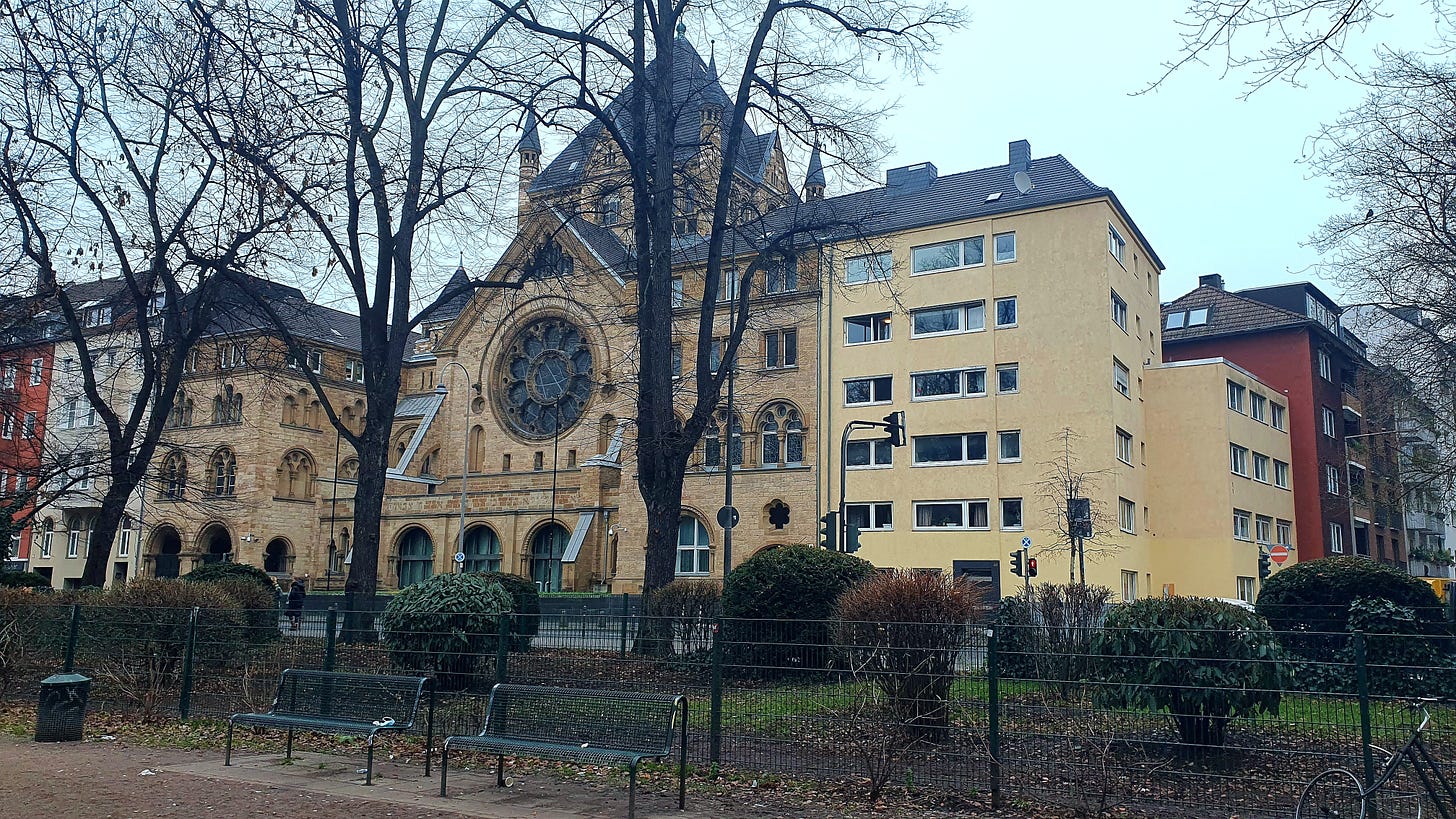 Uma sinagoga, grande e antiga, atrás de umas árvores que já perderam suas folhas neste início de outono