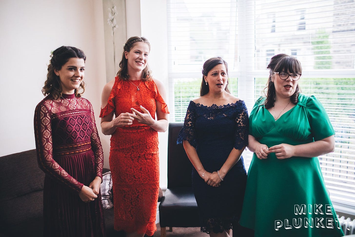 Four women in bright coloured dresses reacting to seeing the bride for the first time just out of shot. Smiles/ emotion on their faces