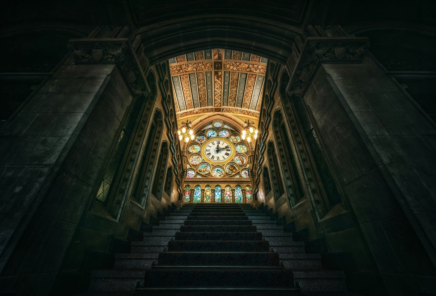 A very dark stone staircase leading up to a wall of ornamental stainglass windows with a large clock in the middle. A very dark stone staircase leading up to a wall of ornamental stainglass windows with a large clock in the middle.