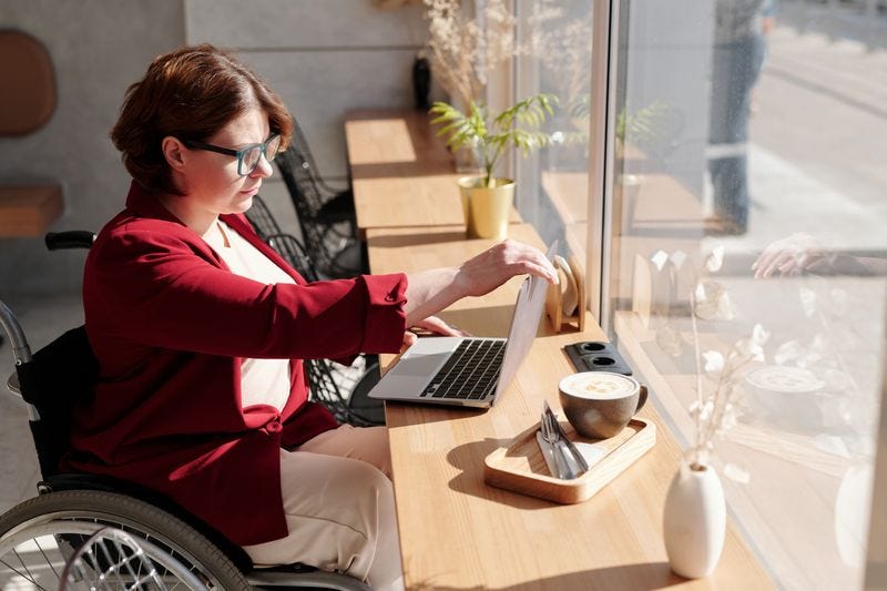 Person working in a cafe at a laptop, using a wheelchair