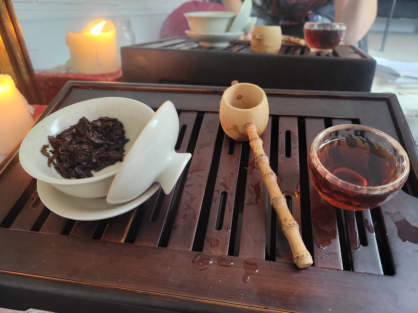 gaiwan with leaves in it, cup of dark tea, bamboo strainer all on a tea tray