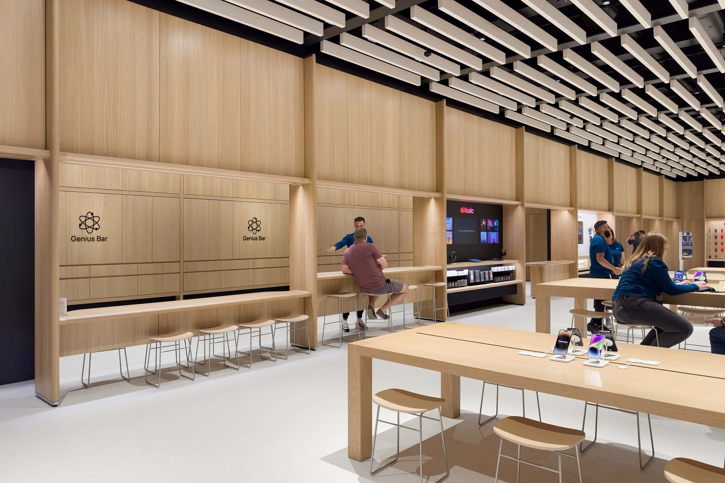 Customers sit at the Genius Bar and high table along the back wall of Apple Battersea.