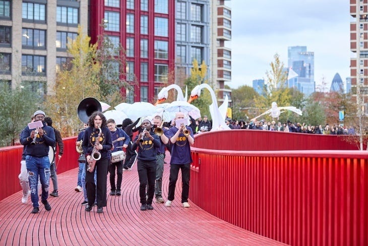 Musicians and swan puppets parading over a red footbridge