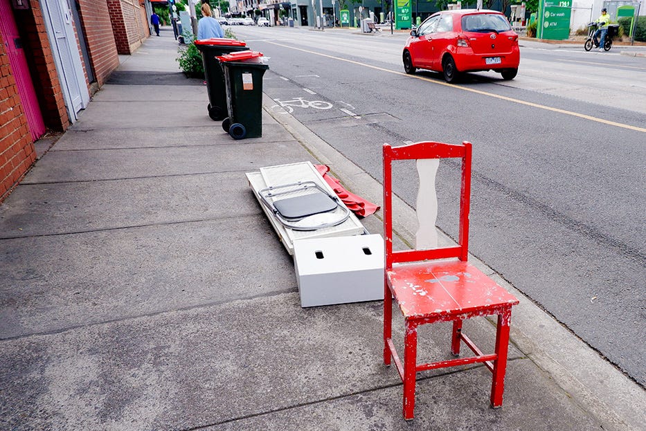 A red chair with a red car in the background and some red topped bins too.