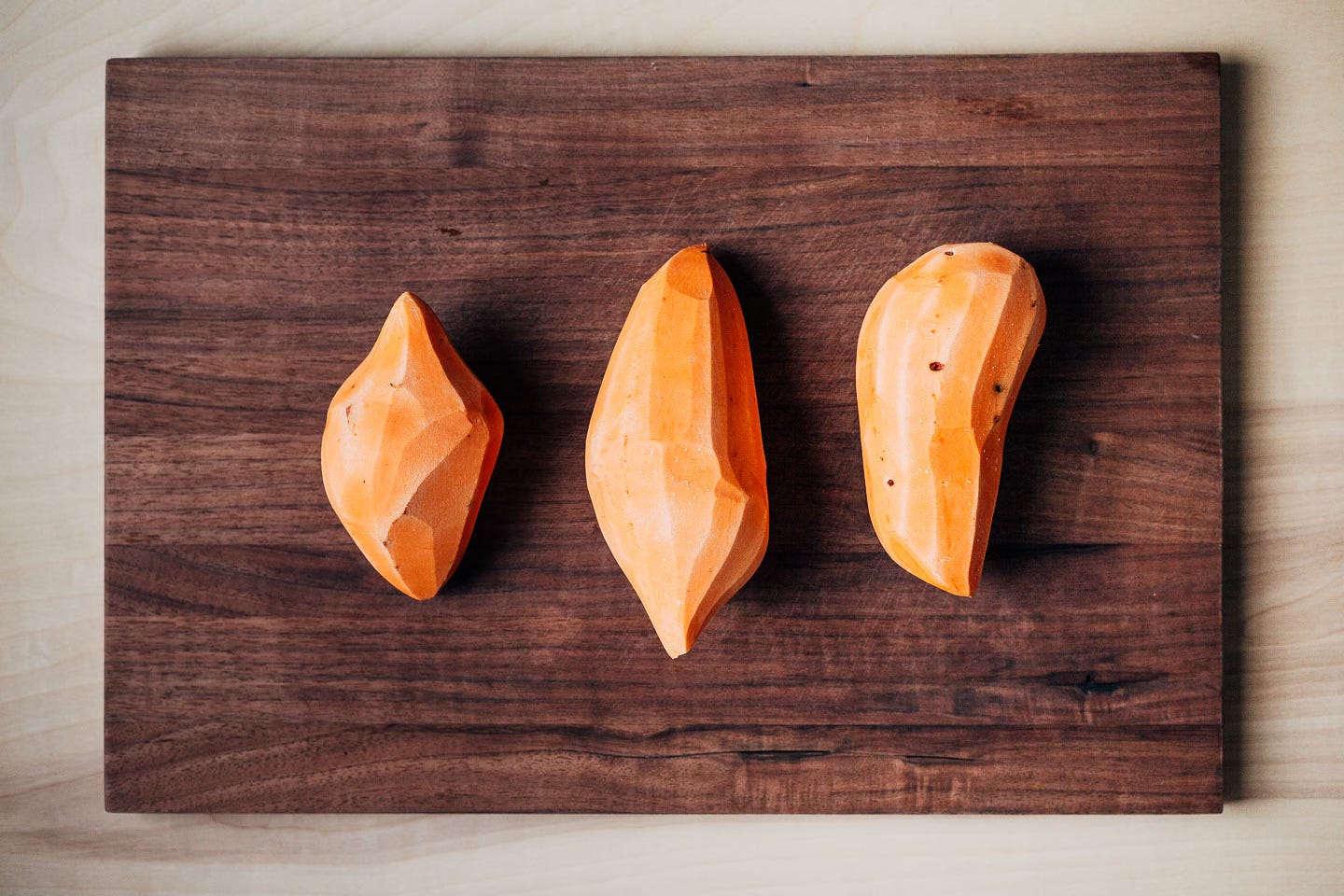 Three peeled sweet potatoes on a cutting board