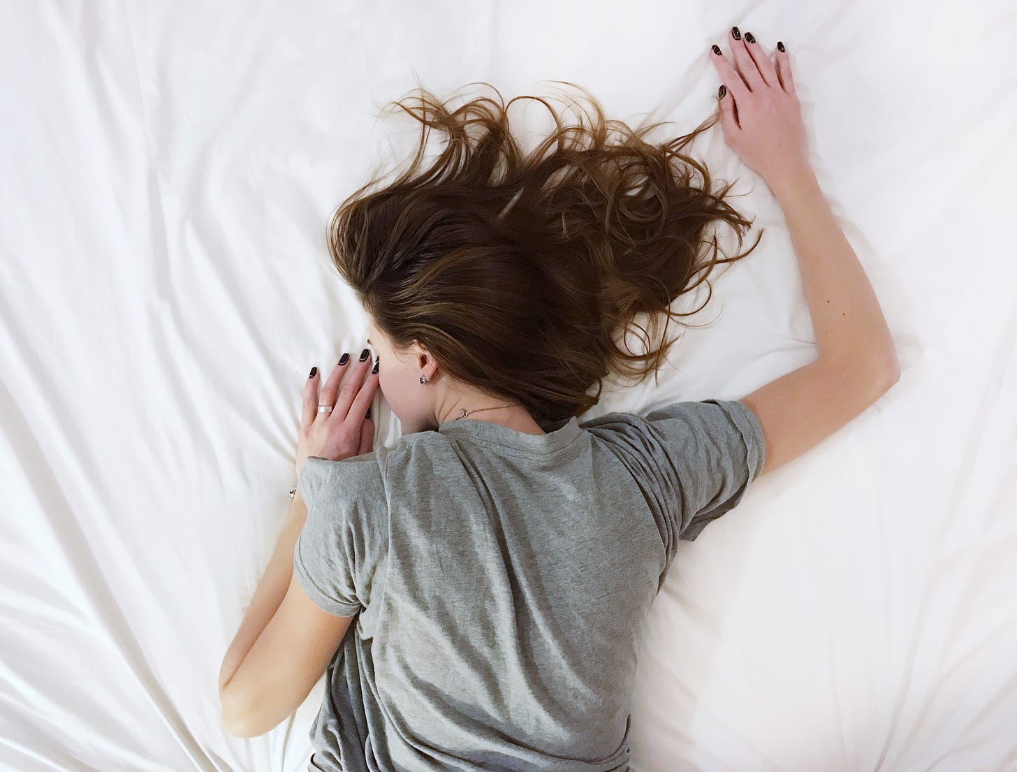 Exhausted woman face down on bed with white sheets