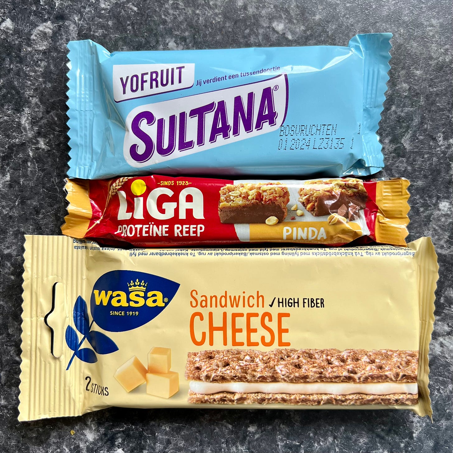 Three snack bars from the Netherlands, one called Yo Fruit Sultana, one called LIGA and another called WASA Sandwich Cheese.