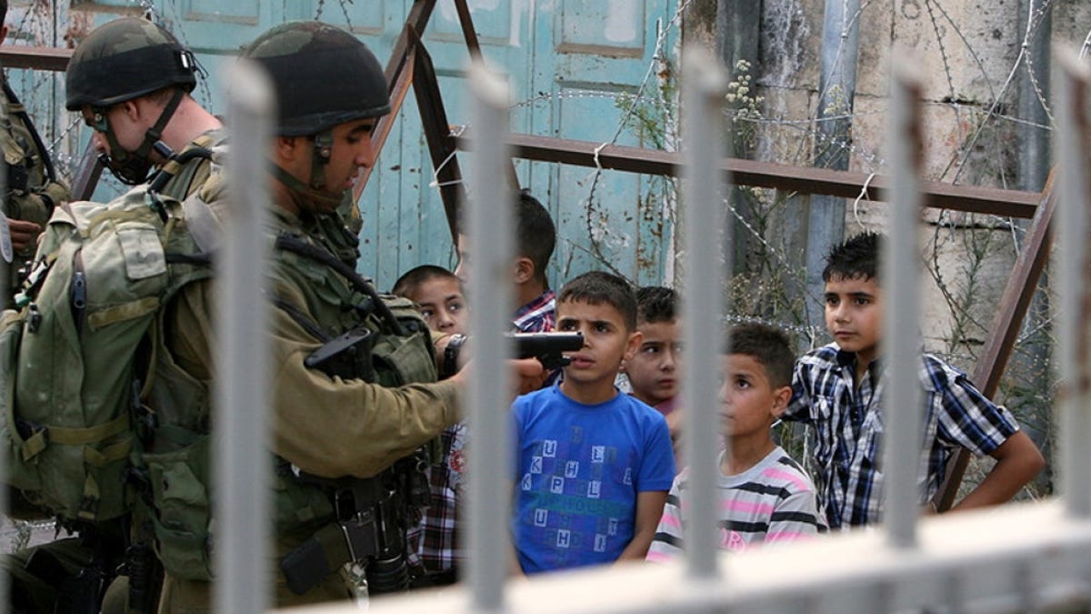 israeli soldiers holding a gun at kids at a checkpoint in occupied palestine