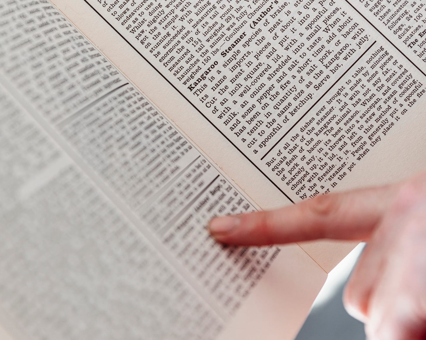 A human finger points to a page of dense printed text