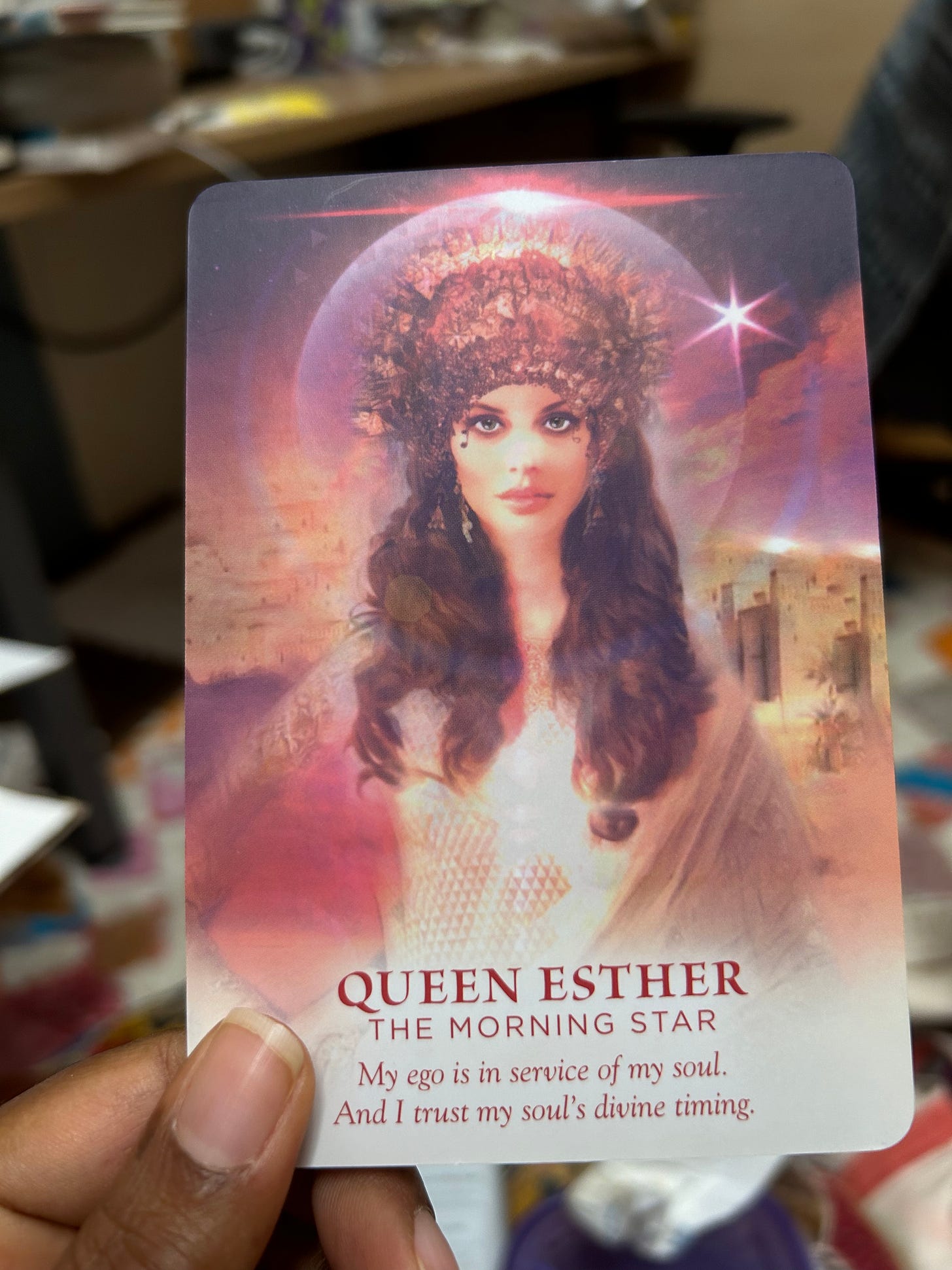 An image of a woman with peach pink skin, long brown hair, and intense eyes. there is a crown on her head. Below the illustration it reads Queen Ester, The Morning Star. My ego is in service of my soul. And I trust my soul's divine timing. 