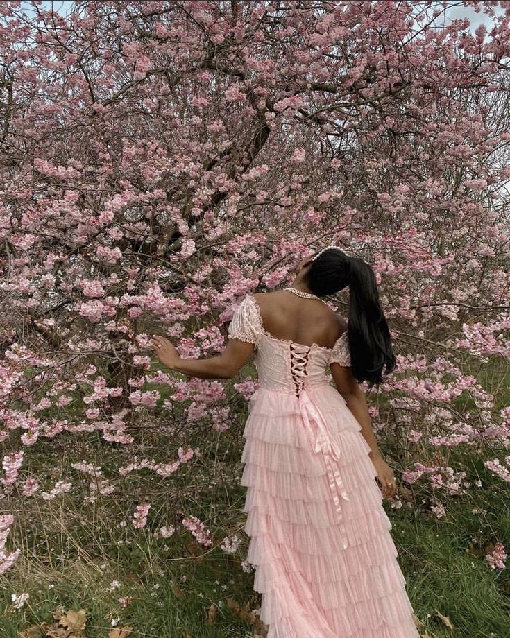 This may contain: a woman standing in front of a tree with pink flowers