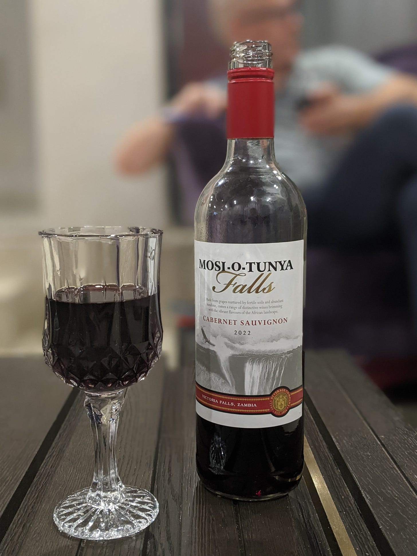 Photo of a bottle of red wine with the name Mosi-o-Tunya. A glass of wine sits next to the open bottle.