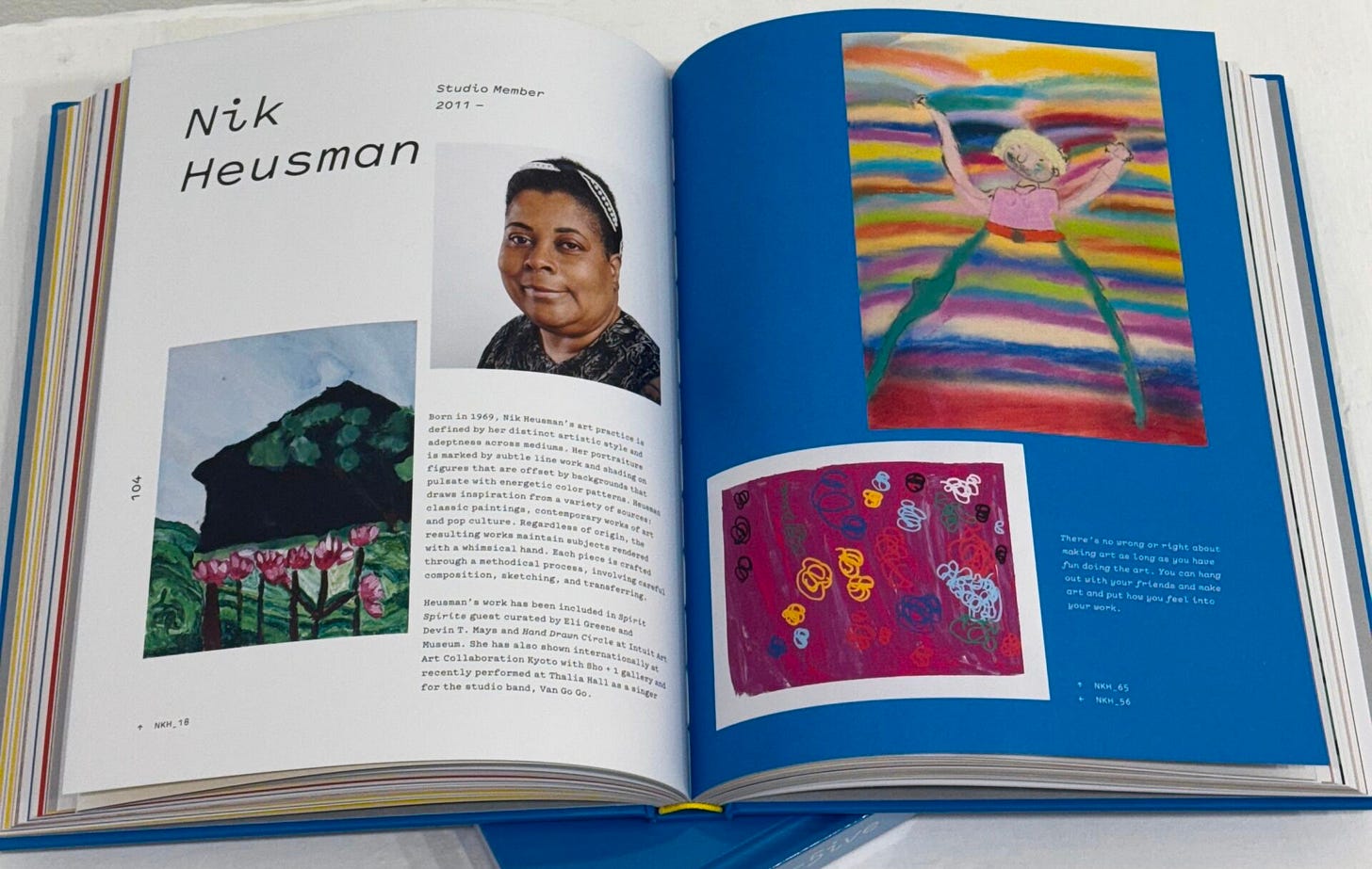 A book is open to a page that says Nik Heusman, Studio Member, 2011 to present. There is a photo of Nik, a Black woman with short hair, and images of her art works with small text describing her work.