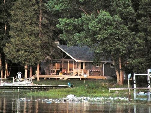A cabin surrounded by pines viewed from a lake.