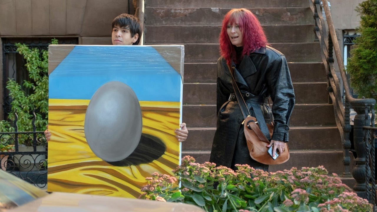 Julio Torres holds an oil painting of an egg next to Tilda Swinton in "Problemista" (2024)