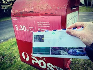 An envelope decorated with old wrapping paper is posted in a red Australia Post letterbox