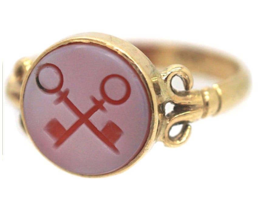 gold swirl ring with round pink stone engraved with two red crossed keys