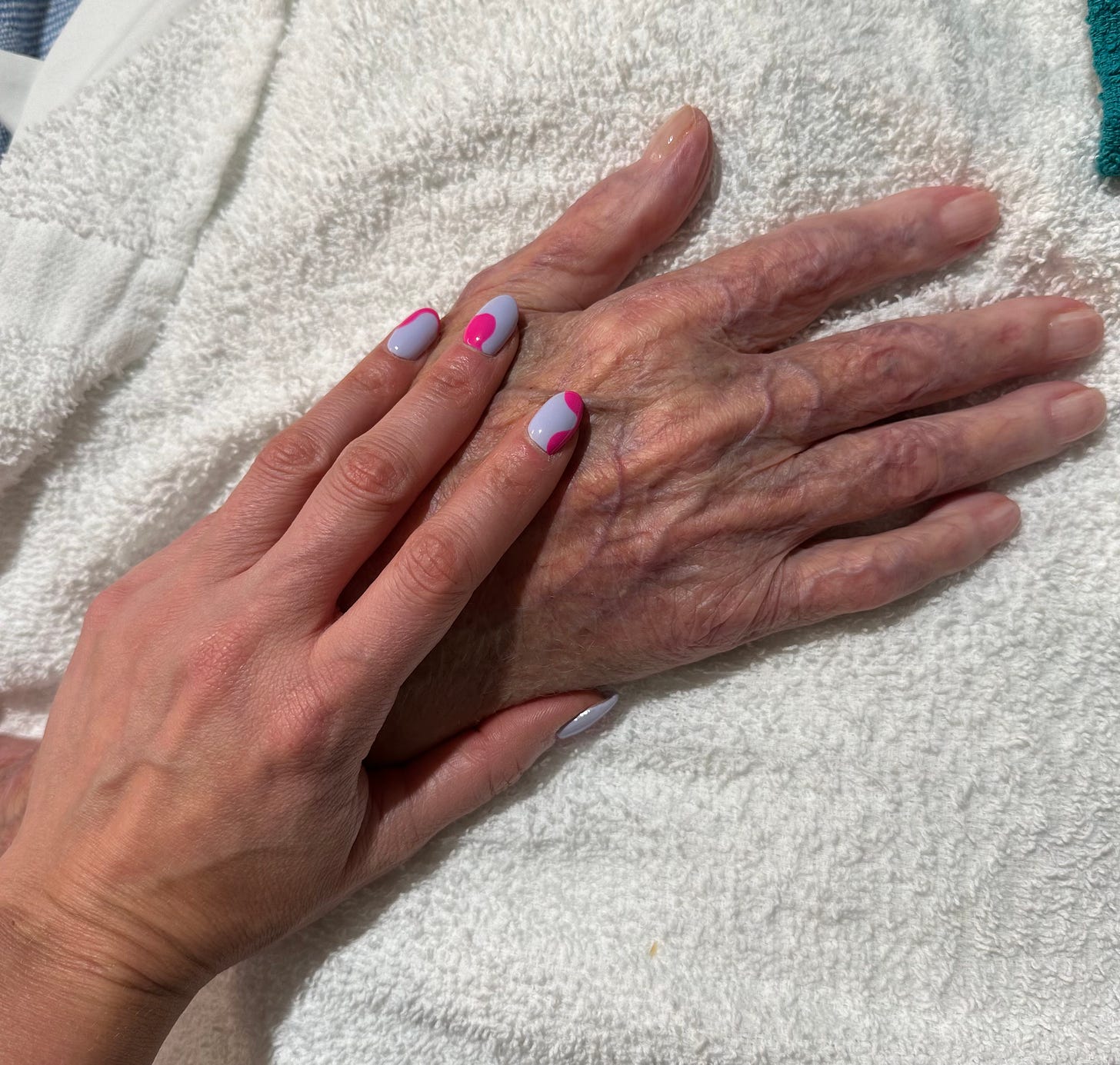 A white woman's left hand lies on top of an elderly white man's right hand.