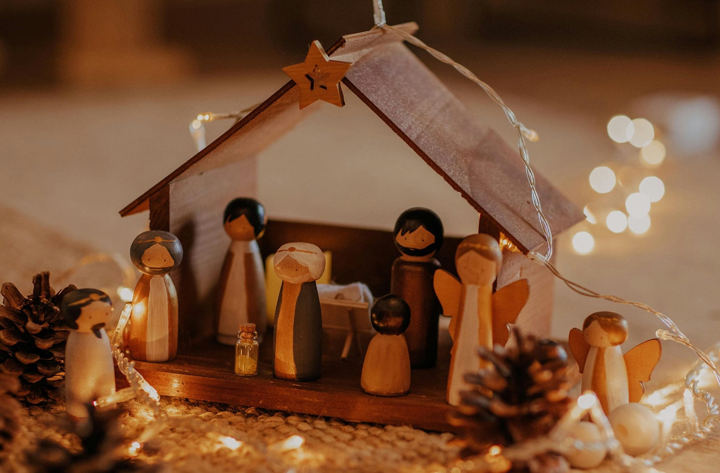 Free A wooden nativity scene surrounded by warm Christmas lights and pinecones. Stock Photo