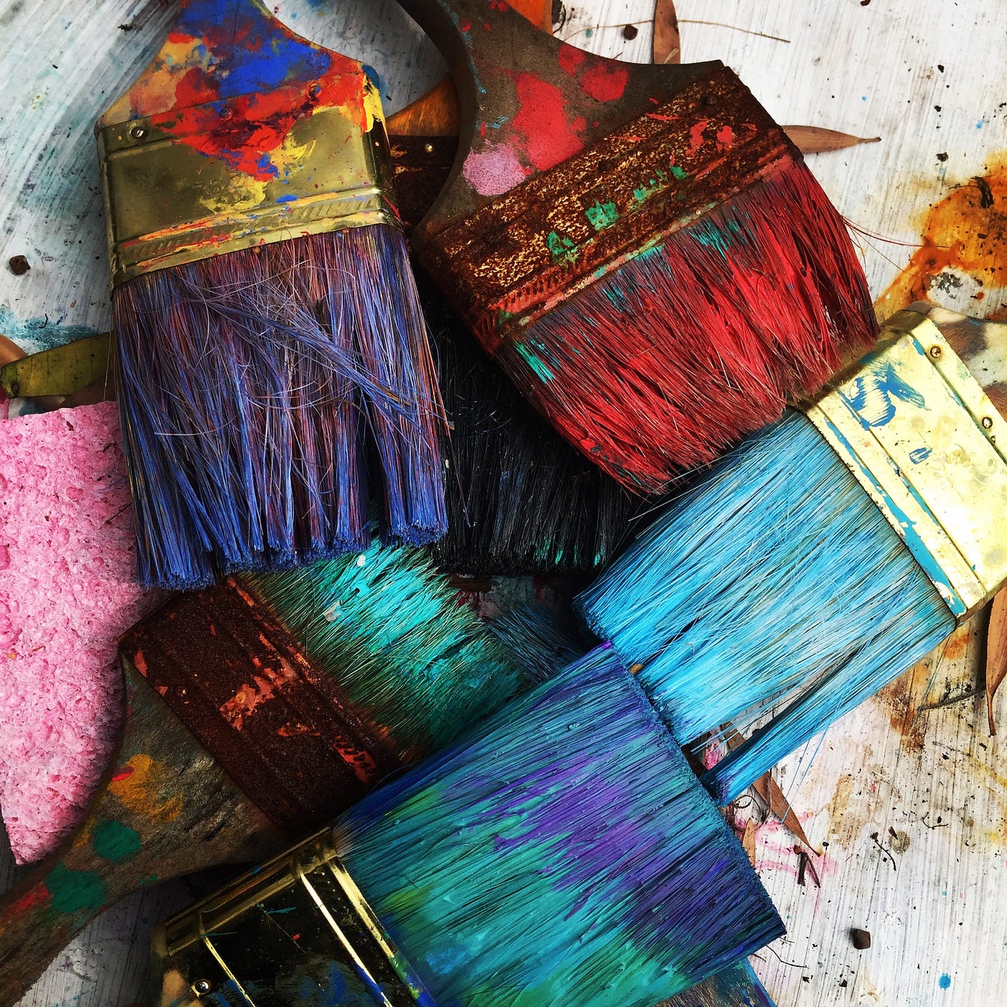 Close-up of an array of wide paint brushes, dipped in ombres of blue and teal, purple and orange. 