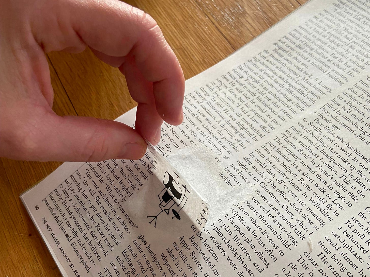 A hand is peeling tape off of a magazine, bringing up an image of a drum set off the page.