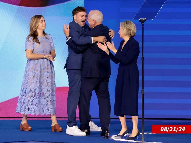 The Walz family embracing joyfully on stage at the DNC Convention against a blue background.