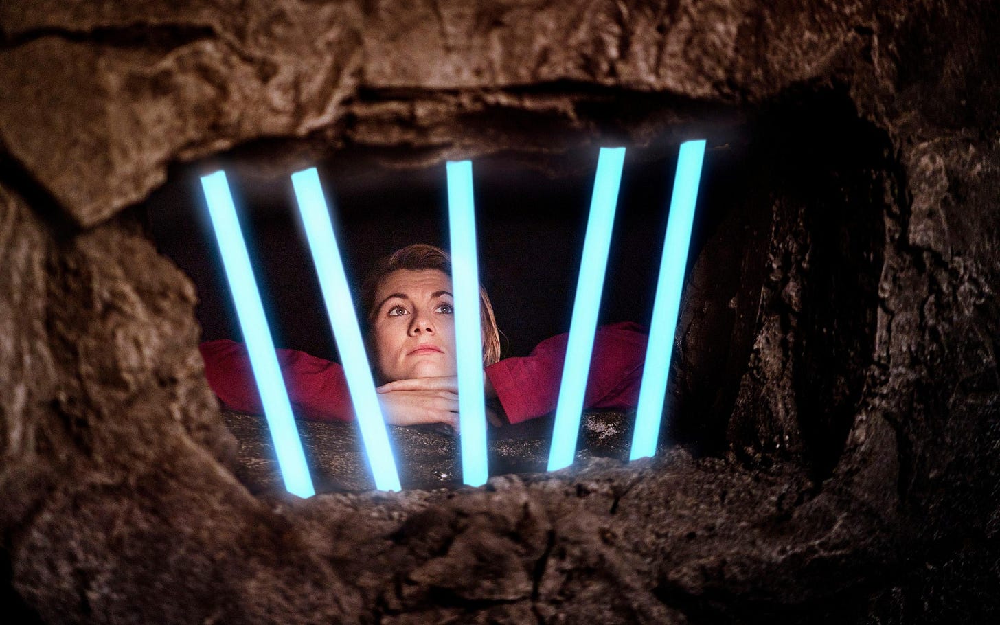 This image shows the Thirteenth Doctor (played by Jodie Whittaker) listlessly gazing through the laser bars of her Judoon prison cell in "Revolution of the Daleks" (Doctor Who's 2021 New Year's Day Special). Dressed in a red jumpsuit, the Doctor's cell is set in the rocky face of an asteroid located somewhere in Judoon space. This image shows the Thirteenth Doctor (played by Jodie Whittaker) listlessly gazing through the laser bars of her Judoon prison cell in "Revolution of the Daleks" (Doctor Who's 2021 New Year's Day Special). Dressed in a red jumpsuit, the Doctor's cell is set in the rocky face of an asteroid located somewhere in Judoon space.