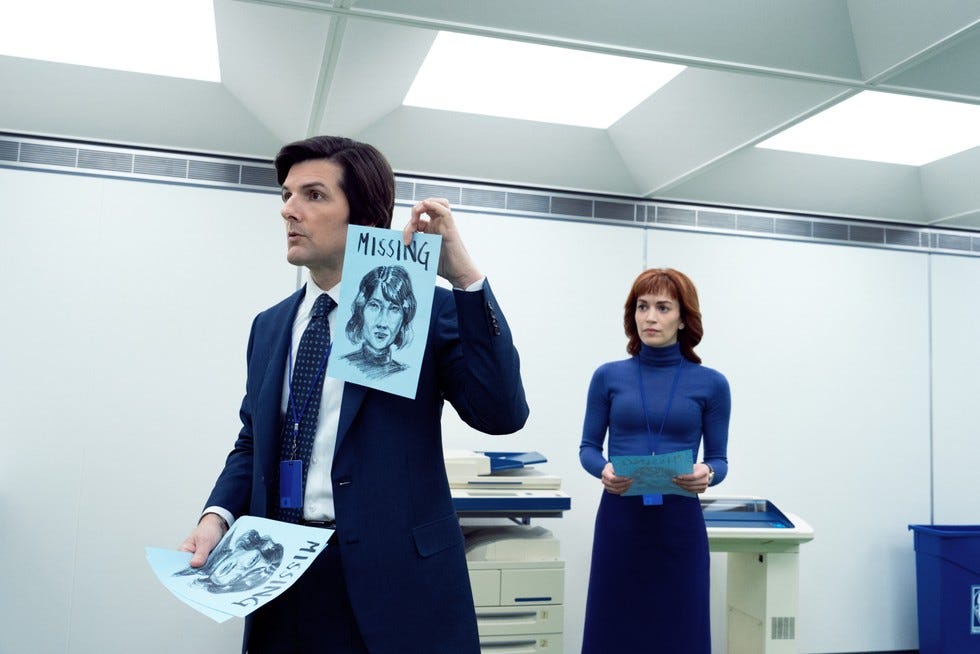 Mark S (Adam Scott) holds up a hand-drawn poster of his missing wife as he stands next to a photocopier, with Helly R (Britt Lower) watching