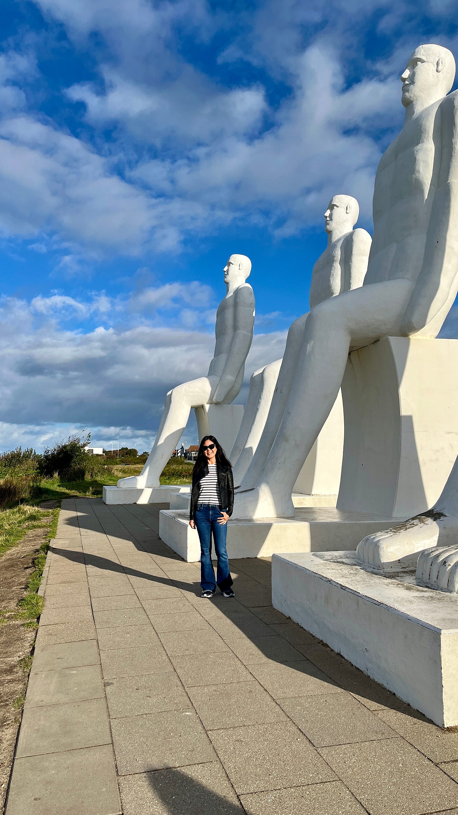 Evelyn Skye next to towering white statues of naked men, facing the sea