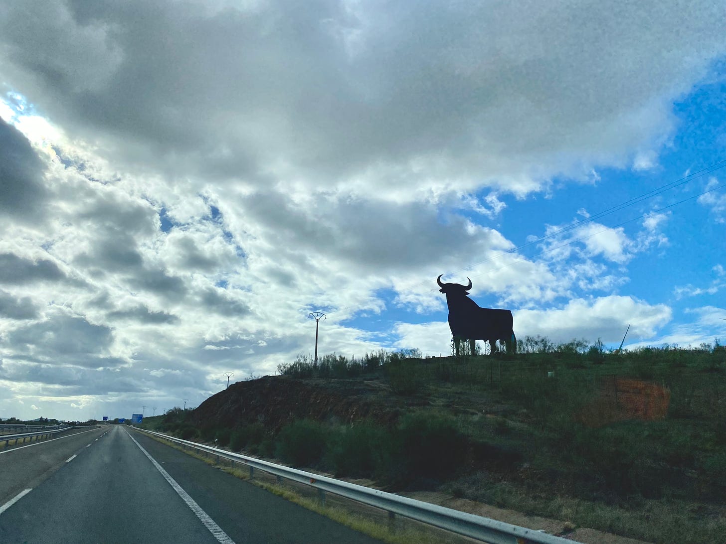 A bull silhouette sculpture on a small hill next to a motorway