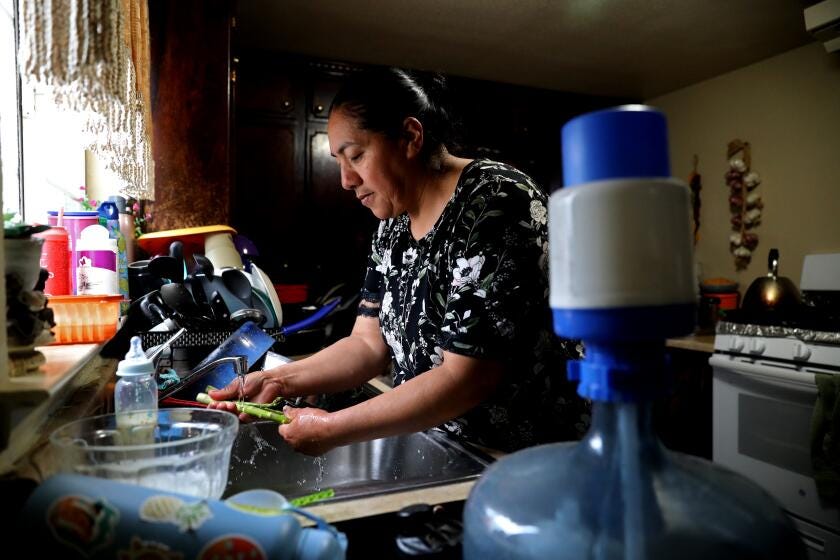 SANGER, CA - FEBRUARY 21: Carolina Ledesma-Garcia, 48, homeowner over 14-years, washing asparagus, lives with her husband and five children, in a house that relies on non-potable water to be delivered to a 2500-gallon tank on their property, along Cottle Ave. in the Tombstone neighborhood, unincorporated Fresno County, on Tuesday, Feb. 21, 2023 in Sanger, CA. Ledesma-Garcia's water well, shown right, went dry in 2019. She signed up with Self Help Enterprises who transport non-potable water to a 2500 gallon tank located on her property. In the community of Tombstone in Fresno County, residents' wells have continued going dry during the drought as nearby farms have heavily pumped groundwater, drawing down the water levels. Residents have lost access to water and are now depending on tanks and deliveries of water by truck. A potential solution for the area would involve connecting to water pipes from nearby Sanger, but progress has been slow. (Gary Coronado / Los Angeles Times)