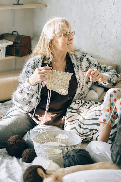 Free A senior woman enjoys knitting while sitting with family in a cozy home setting. Stock Photo