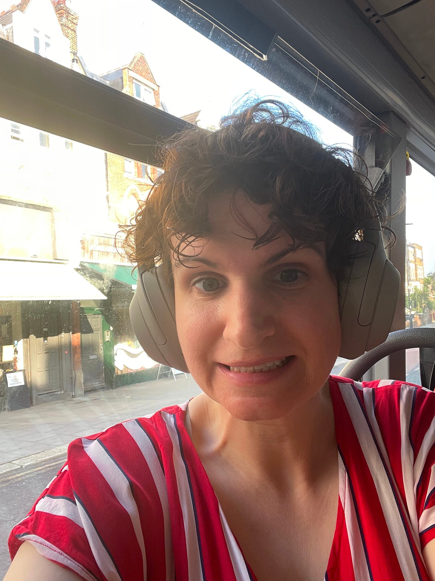 Emily, a white person with short, curly brown hair, smiling for a selfie on the bus