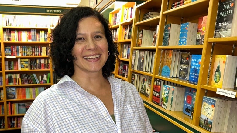 A woman standing next to a wall of books.