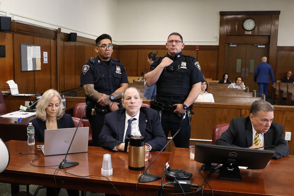 Harvey Weinstein, in a dark suit and tie, sits in court with his lawyers, Diana Fabi Sampson and John Esposito. 