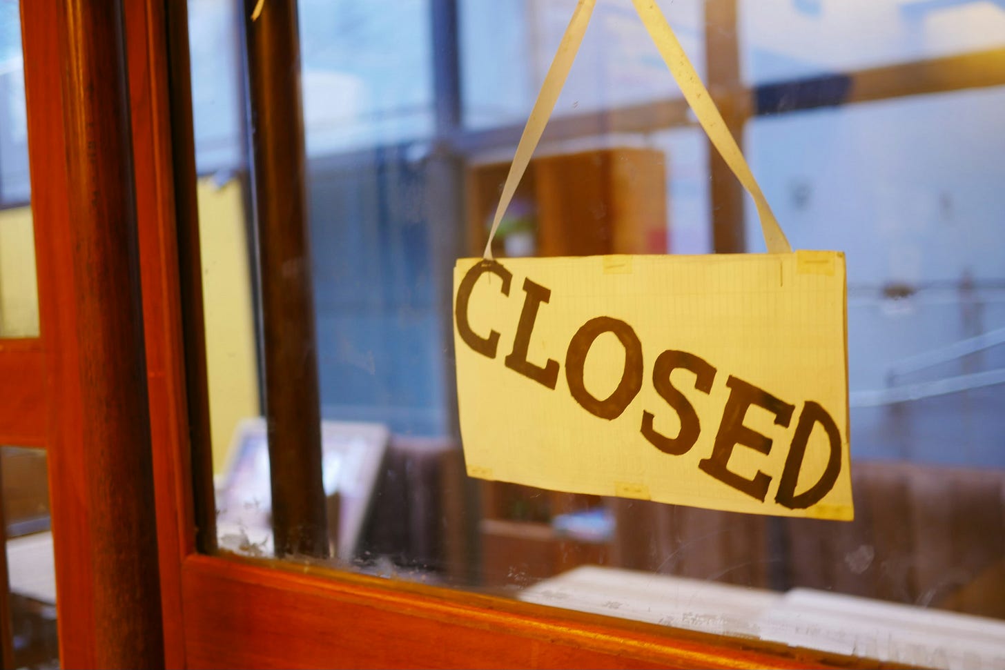 A red shop door with a yellow sing in the door's window which says closed