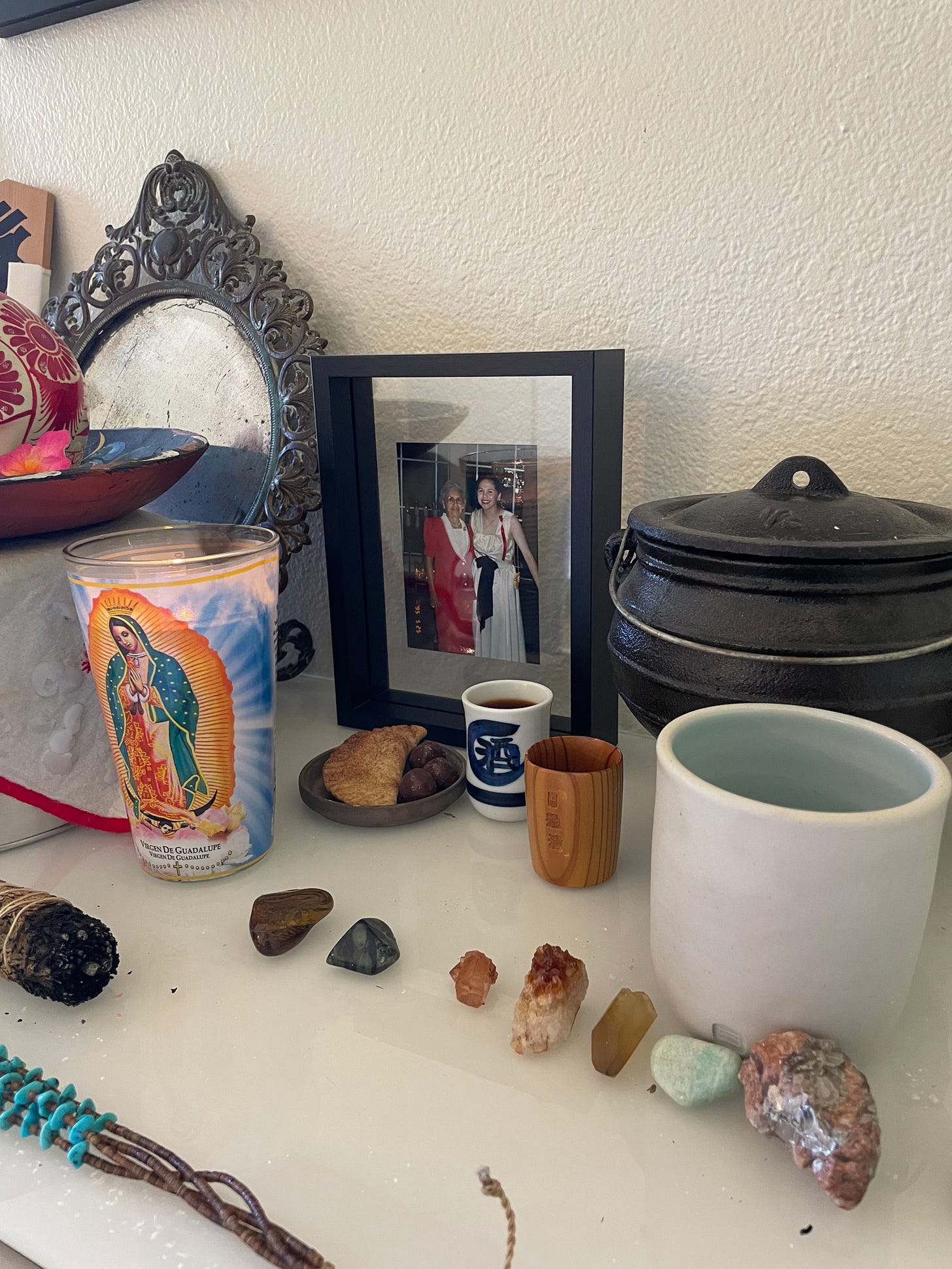 an up-close detail of home altar with a family photograph, small containers with liquids, and small amounts of food