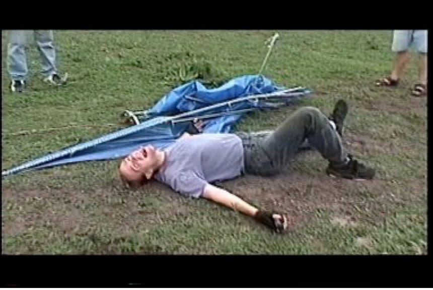 Bob lies on the ground next to the wreckage of a homemade hang glider.