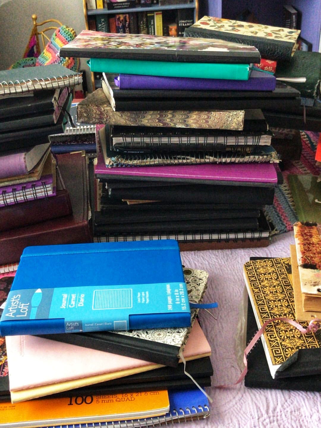 Maybe about 50 blank books and notebooks in several piles on a bed
