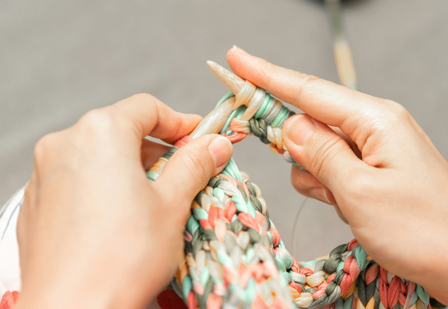 Hands holding knitting needles with variegated yarns in greens and oranges