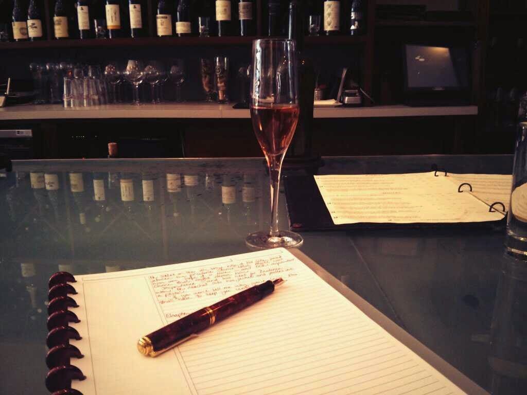 A wine bar top with a champagne glass, a notebook, and a fountain pen