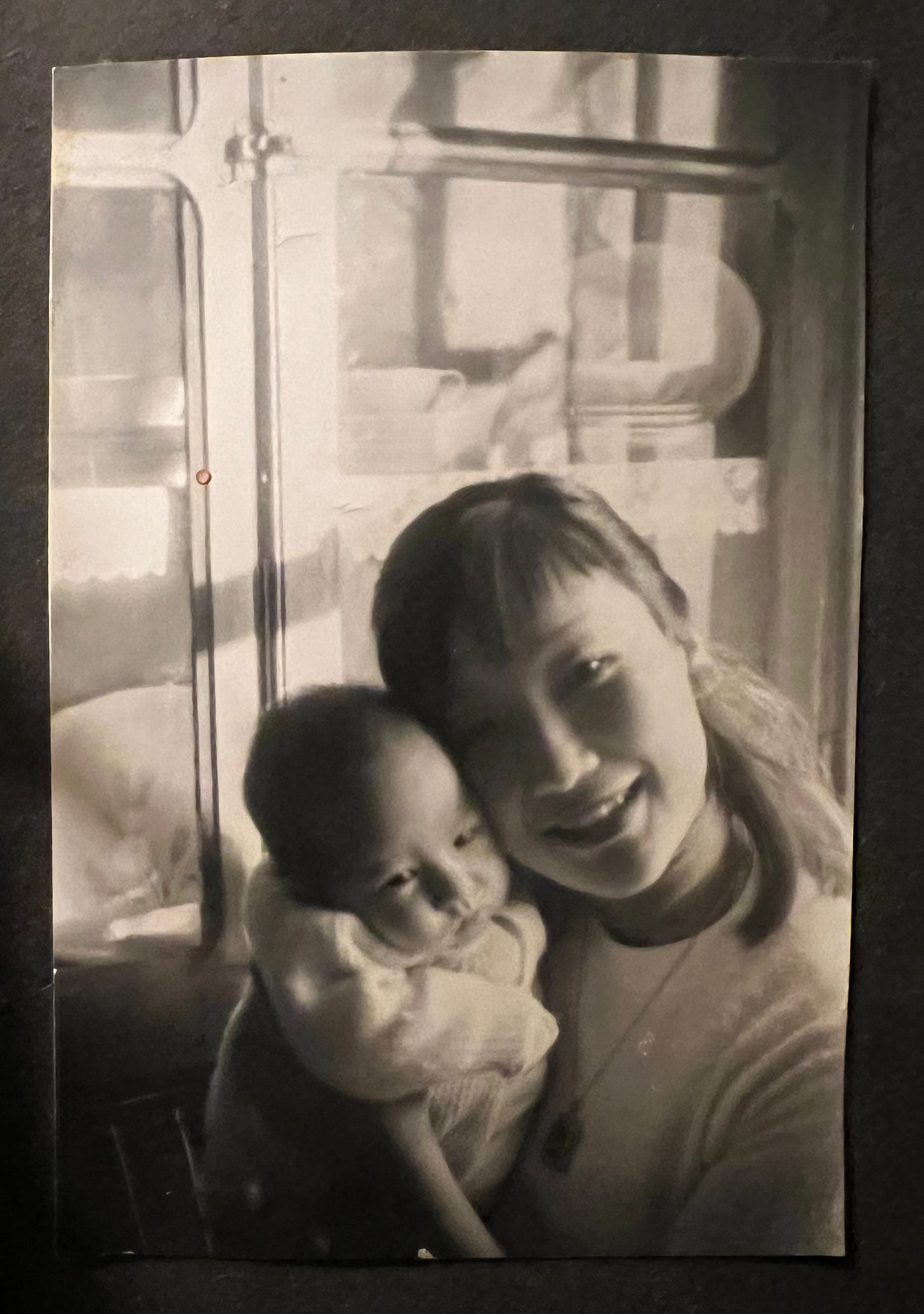 Old photo of demian, as an infant, in her mother's arms, smiling at the camera