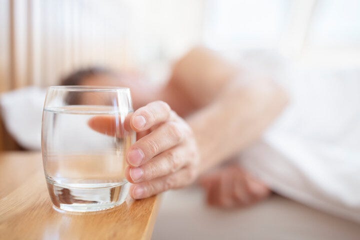 Glass of fresh drinking water on bed bedside table