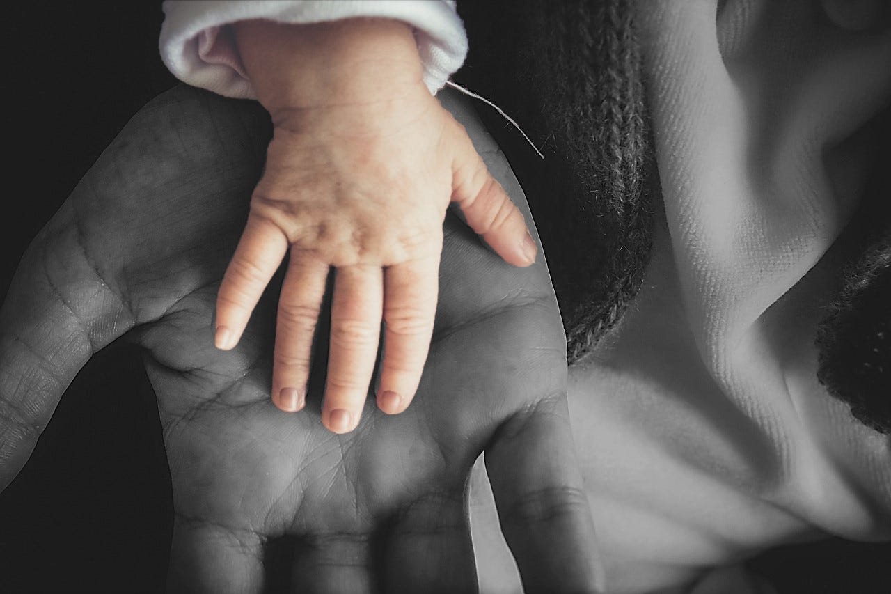 A child's hand in color over a black and white photo of a father's hand